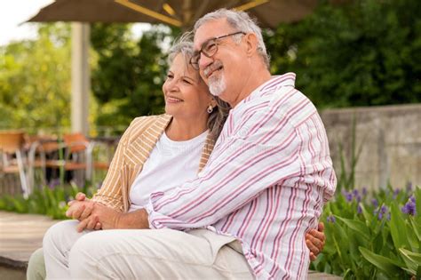Smiling Senior Caucasian Husband Hugging Woman In Casual Sit On Bench