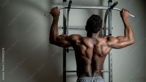 African American Man With Naked Torso Pulls Up On Horizontal Bar In Gym