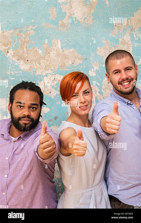 Young Multiethnic People Posing In Front Of A Grunge Wall With A Thumbs