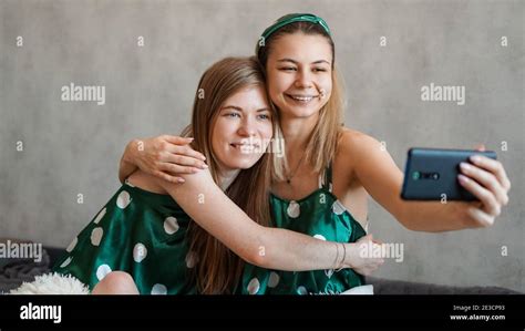 two beautiful happy girlfriends hugging and taking selfies with smartphone at pajama party stock