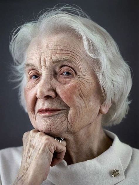 an older woman with white hair and blue eyes is looking at the camera while she has her hand on
