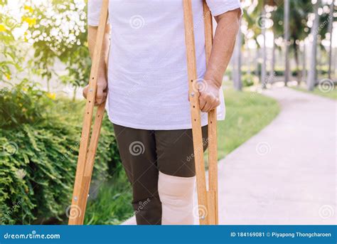 Patient Elderly Woman Using Crutches Support Broken Legs For Walking At