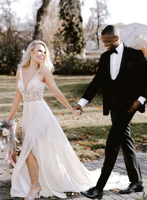 A Bride And Groom Hold Hands As They Walk Through The Park