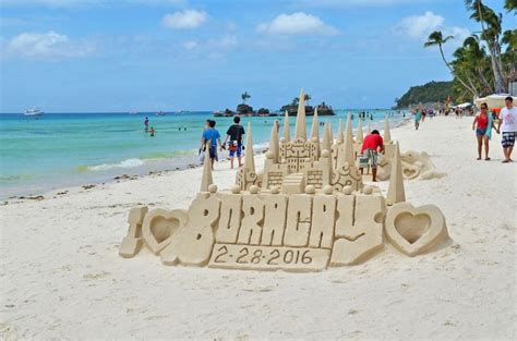 A Sand Castle On The Beach With People Walking Around