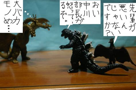 Two Godzilla Figurines On A Wooden Table With Japanese Characters In