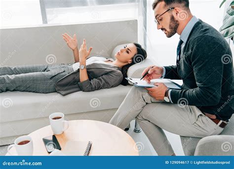 Female Patient Lying On Sofa And Talking With Psychologist Stock Image
