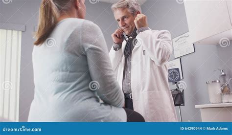 Male Senior Doctor Listening To Patient Vitals With Stethoscope Stock