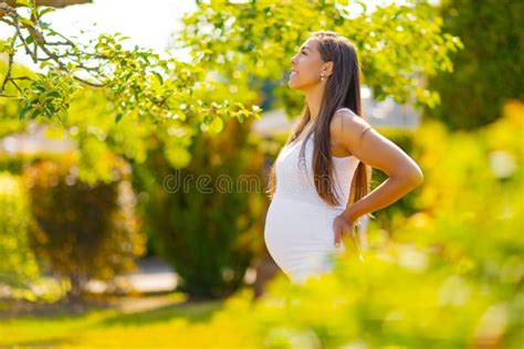 Happy Pregnant Woman Standing In Garden Holding On Tummy Stock Photo