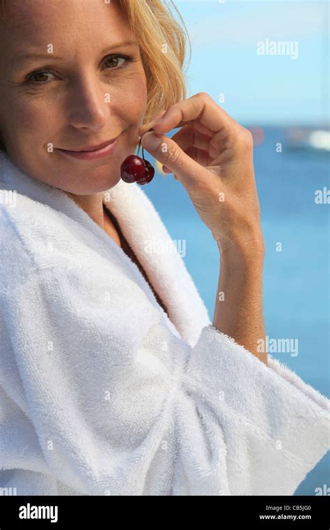 50 years old blonde woman dressed in bathrobe in front of the sea taking cherries in her fingers