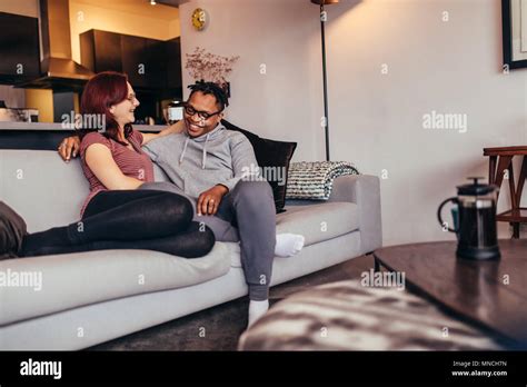 Cheerful Interracial Couple Sitting On A Couch In Living Room Man