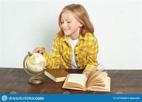 The Student Sits At The Table And Looks At The Globe Near Books And A