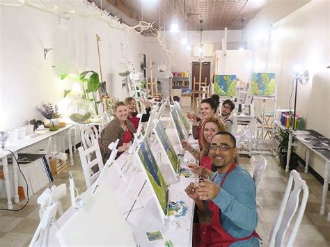 A Group Of People Sitting At A Table With Paintings On The Easels In