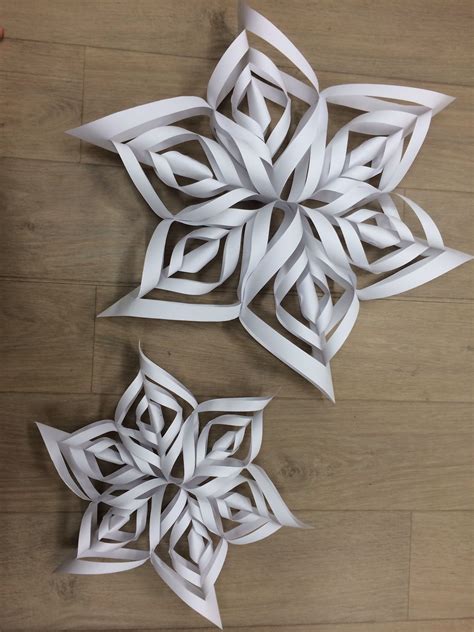 Two Paper Snowflakes Sitting On Top Of A Wooden Floor Next To Each Other