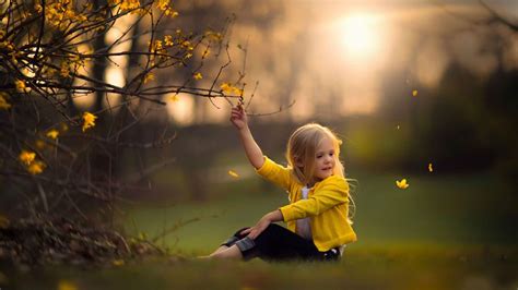 Cute Baby Girl Is Sitting On Green Grass Touching Flower Wearing Yellow