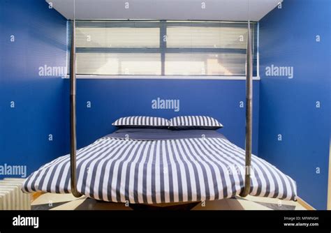 Suspended Metal Bed With Striped Bed Linen Beneath High Window In