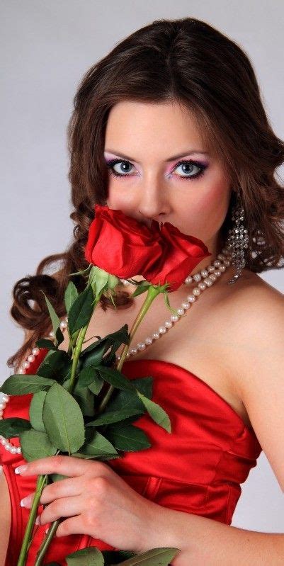 A Woman In A Red Dress Holding A Rose Up To Her Face And Looking At The Camera