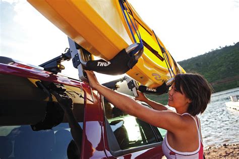 The top deck can carry a kayak up to 34 wide and 75 lbs. A woman loading a kayak to her roof rack using the Thule ...