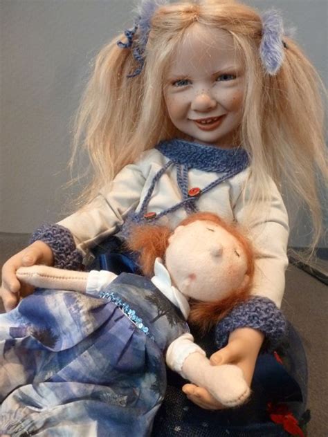 A Doll With Blonde Hair Is Sitting Next To Another Doll