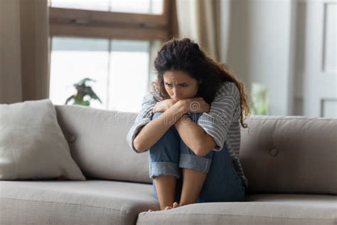 Stressed Young Woman Embracing Knees Sitting Alone On Couch Stock