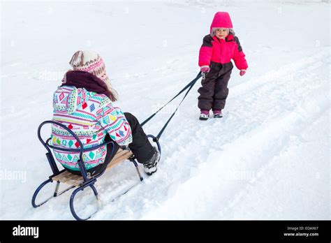 Little Baby Girl In Pink Pulling A Sled With Her Big Sister On Snowy