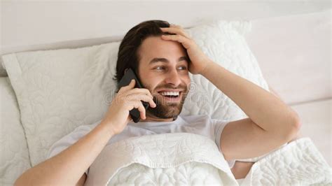 Cheerful Shocked Young Caucasian Guy Lies On Bed Wakes Up Calls By