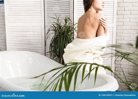 Attractive Young Girl In A White Bathrobe Applies Cream To The Skin While Sitting In The