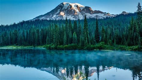 Snow Capped Mountain Surrounded With Trees Near Body Of Water With