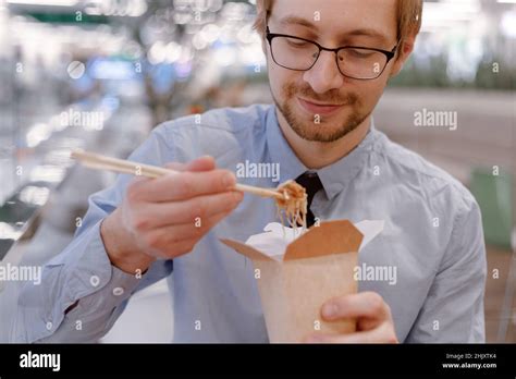 Young Businessman With Chopsticks Eating Chinese Wok From Box On Food