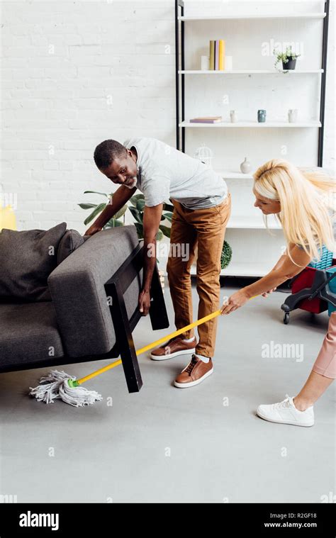 Blonde Woman Cleaning Floor With Mop While African American Lifting Up