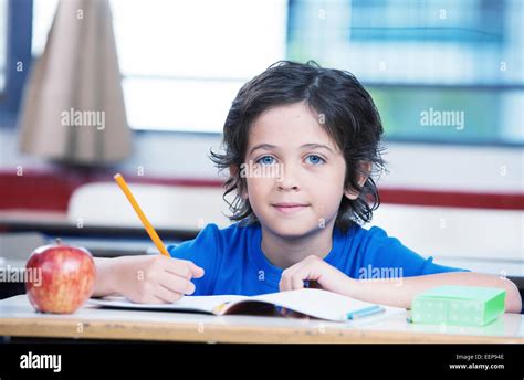 Kid At School Writing On His Book With An Apple On The Desk Stock Photo