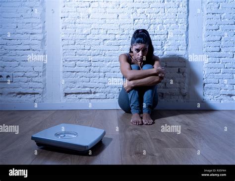 joven adolescente bulímica anoréxica mujer sentada sola en el suelo mirando la escala preocupado