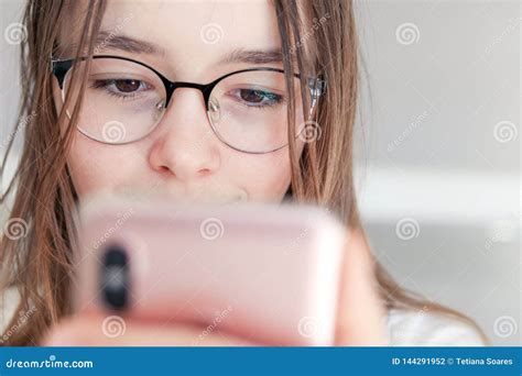 close up portrait of cute happy tween girl in glasses looking at smartphone in her hands stock