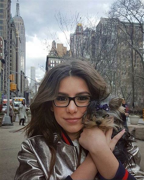 A Woman Holding A Small Dog In Her Arms On A City Street With Tall