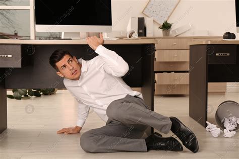 Scared Man Hiding Under Office Desk During Earthquake Stock Photo