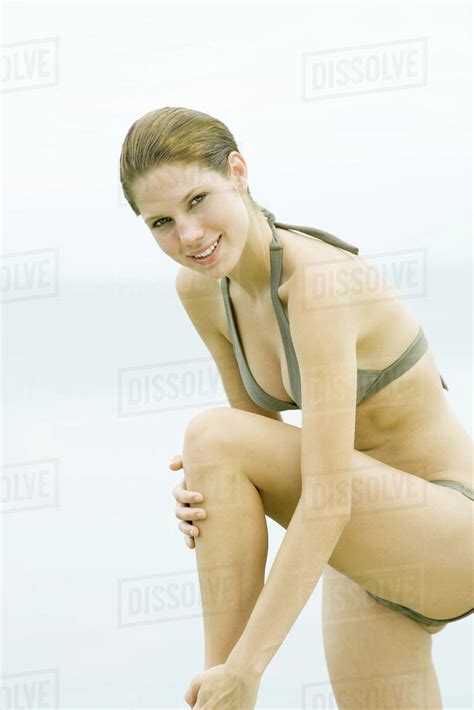 Young Woman In Bikini Standing With One Knee Up Touching Leg Smiling