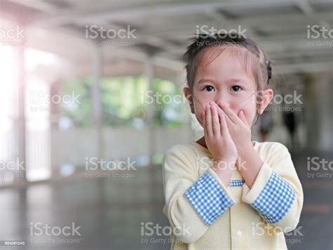Little Asian Girl Covering Her Mouth And Nose With Her Hands Stock