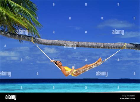 Woman Relaxing In Hammock Under Palm Tree And Blue Skies With Tropical
