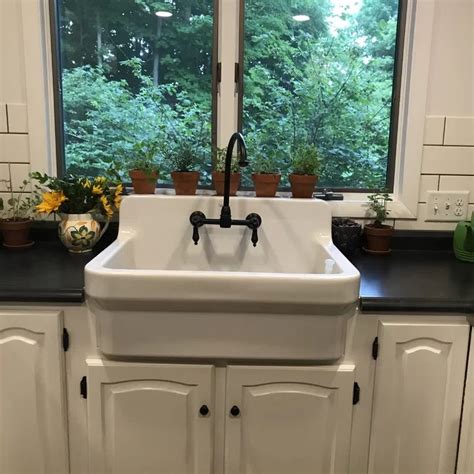 A Kitchen Sink Sitting Under A Window Next To Potted Plants And Pots On