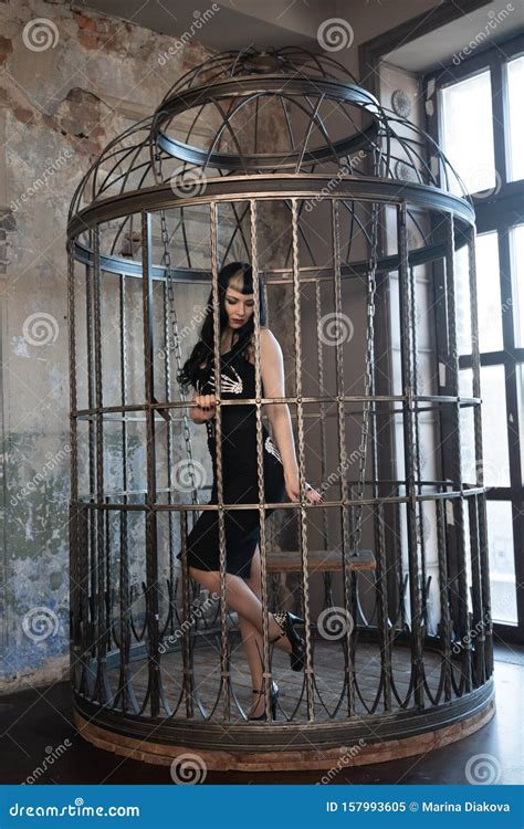 gothic girl in tight black dress behind the big cage posing as slavery victim alone stock image