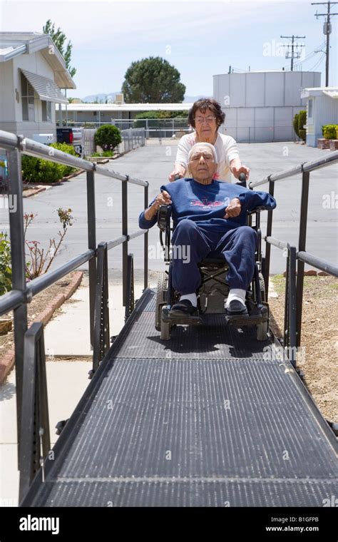 Senior Hispanic Woman Pushes Her Handicapped Husband Up The Ramp To