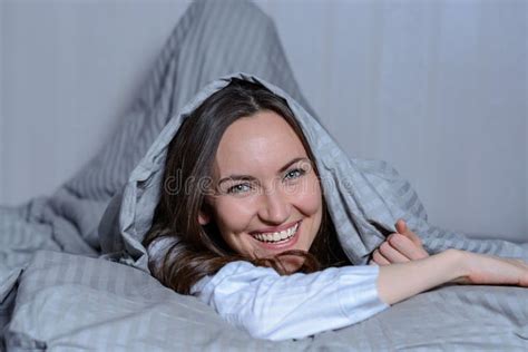 A Young Beautifully Laughing Woman Is Lying In Bed Under A Blanket