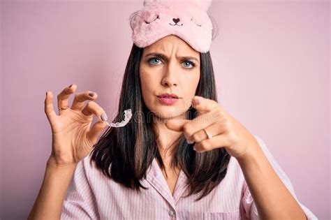 Young Brunette Woman With Blue Eyes Wearing Pajama Holding Dentist Clear Aligner Pointing With