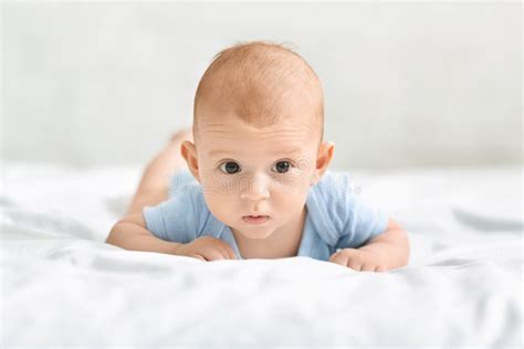 Portrait Of Curious Newborn Baby In Diaper Lying On Bed Stock Photo