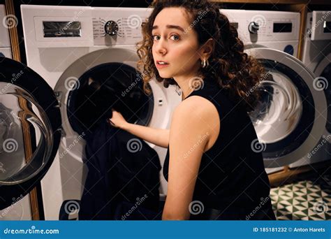 Pensive Brunette Girl Washing Clothes In Self Service Laundry Stock