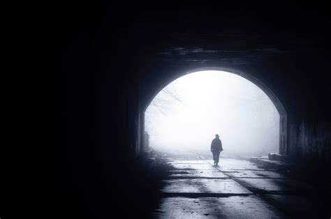 Silhouette Of Person Walking Through A Dark Tunnel As Light Shines