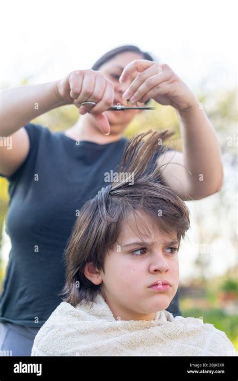 mother cuts her son s hair in the garden at home the mother is a hairdresser for her son stock