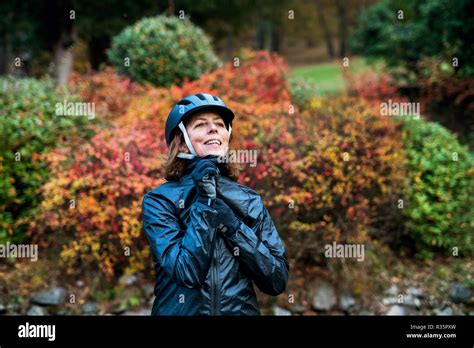 Active Senior Woman Standing Outdoors On A Road In Nature Putting On Bicycle Helmet Stock Photo