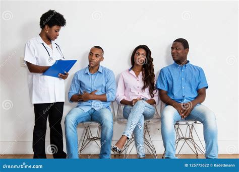 African American Nurse Talking With Patients At Waiting Room Stock