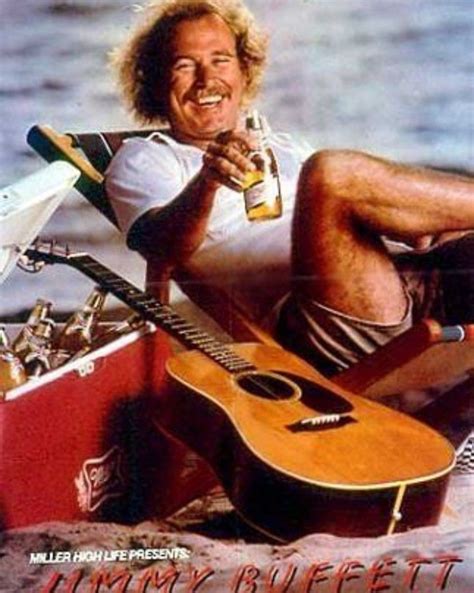 A Man Sitting On The Beach With A Guitar And Beer In His Hand While