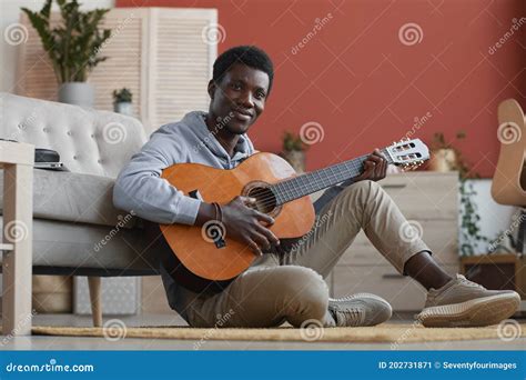 Smiling African American Man Playing Guitar Sitting On Floor Stock
